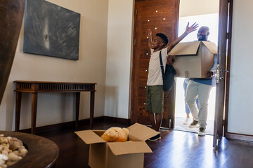 Father and son entering new home, carrying boxes and smiling with excitement