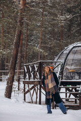 A beautiful woman is relaxing in the forest in winter glamping on the background of a domed tent