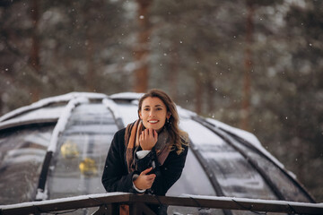 A beautiful woman is relaxing in the forest in winter glamping on the background of a domed tent