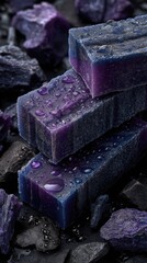 Stacked violet soap bars, wet with water droplets, surrounded by charcoal