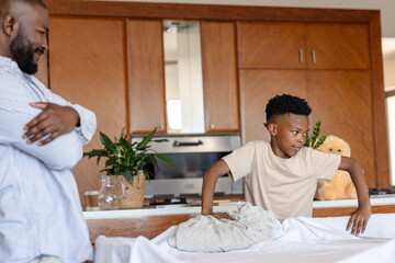 Father watching son folding laundry at home, bonding in kitchen area