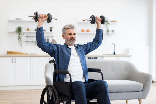 Mature Caucasian man sitting in wheelchair performing exercise with dumbbells in bright home interior, promoting fitness and determination.