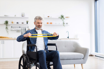 Mature Caucasian man in wheelchair performing stretching exercises using rubber resistance bands within contemporary home environment. Demonstrates independence, fitness focus, and a disciplined