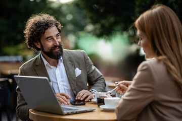 Business people discussing at outdoor cafe with laptop and coffee