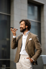 Smiling businessman using smartphone voice assistant outdoors