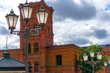 Brick tower and facade of Manufaktura in Ł&oacute;dź, historic industrial architecture, decorative street lamps visible in the foreground.