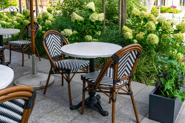 Restaurant garden in Łódź with round tables and woven chairs, surrounded by hydrangeas and decorative greenery.