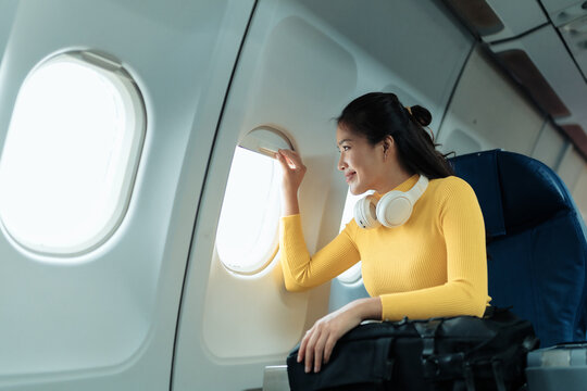 Happy passenger opening airplane window blind while traveling by plane, enjoying the view from above