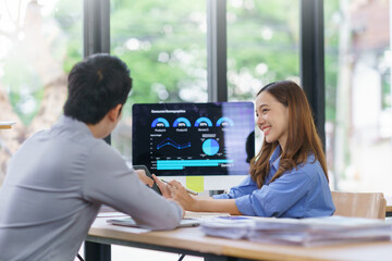 Asian business colleagues analyzing financial charts and discussing data at office desk using computer and tablet