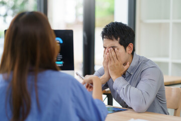 Asian businessman covering his face with his hands, showing stress and frustration during a...