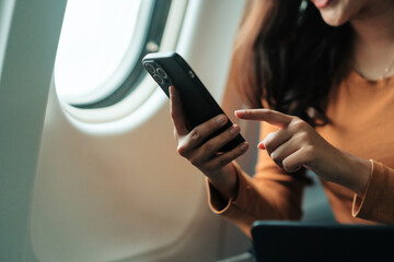 Businesswoman using mobile phone on airplane next to window, browsing internet or watching movies during flight