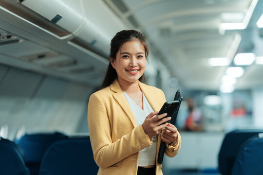Asian businesswoman holding a folder and using a mobile phone while seated in an airplane cabin, enjoying her travel experience