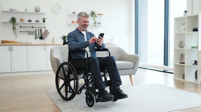 Mature Caucasian man sitting in a wheelchair indoors using smartphone, modern decor visible.