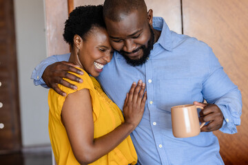 Happy couple embracing at home, man holding coffee mug, sharing joyful moment
