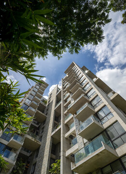 Upward view of a contemporary high-rise featuring concrete and stacked stone walls with balconies on every floor, set against a bright, cloudy sky.
