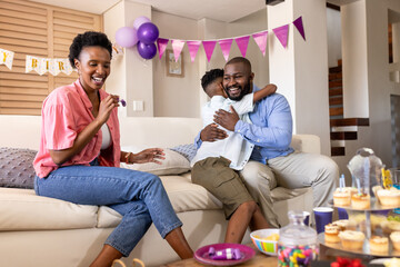 Family celebrating birthday at home, parents smiling while child hugging father