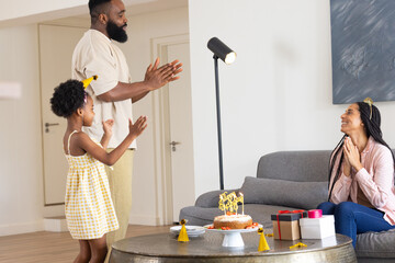 Family celebrating birthday at home, clapping and smiling around cake and gifts