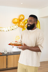 Smiling man holding birthday cake with candles at home celebration