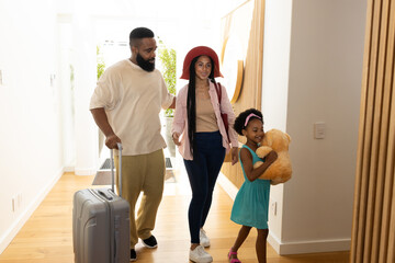 Family arriving home with suitcase, daughter joyfully hugging teddy bear