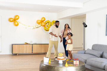 Celebrating birthday at home, joyful family dancing near cake and balloons