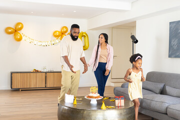 Family celebrating birthday at home, smiling and enjoying cake with decorations