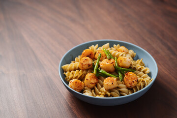 Fusilli pasta with scallops and asparagus in blue bowl on walnut wood surface with copy space