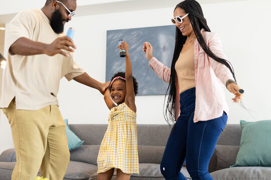 African American family dancing joyfully at home, holding microphones and smiling
