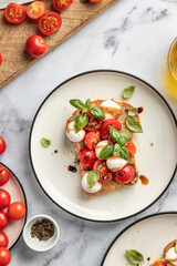 Caprese sandwich or toast with mozzarrella balls, cherry tomatoes, olive oil and fresh basil leaves top view close up on white marble background