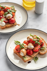 Caprese sandwich or toast with mozzarrella balls, cherry tomatoes, olive oil, pepper and bazil leaves. Healthy vegetarian snack or lunch. White marble background
