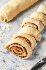 Cutted roll of dough on white marble background. Making cinnamon rolls process. Cinnabon preparation