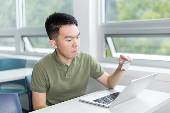 Young man holding up an ID card in front of a laptop, completing an online identification process. - Powered by Adobe