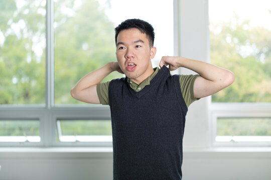 Young teenage boy adjusting a dark sweater vest over a green golf shirt while getting dressed indoors, mid motion with a focused expression. Getting ready for school.