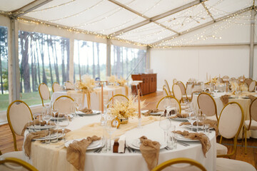 Decorated wedding hall with round tables, string lights and floral arrangements.