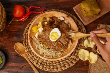 Traditional Indonesian kupat tahu: rice cake, tofu, bean sprouts, and boiled egg served with rich peanut sauce and crunchy crackers on a rustic wooden background.