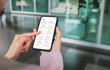 Businesswoman using smartphone with monthly calendar to plan 2026 activities. Scheduling and organizing plans. Technology and business concept.