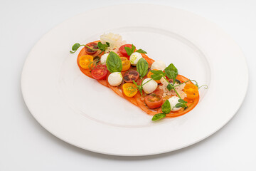 Plated tomato and mozzarella arrangement garnished with basil and herbs