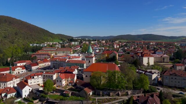 Drone flies toward the historic Kostel svateho Vaclava Church in Tisnov, South Moravia, Czechia, highlighting the town's architecture and the surrounding green Boskovice Furrow hills.