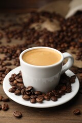 Aromatic coffee in cup and beans on wooden table, closeup