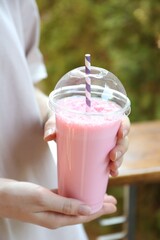 Woman holding tasty milkshake in plastic cup outdoors, closeup