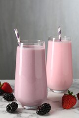 Tasty milkshakes in glasses and berries on white marble table