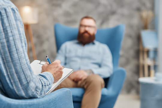 Psychologist taking notes while listening to patient during therapy session