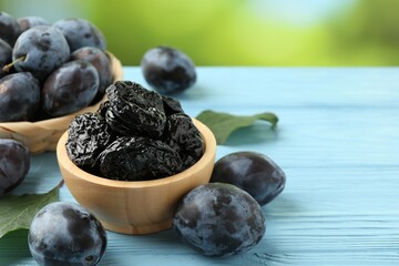 Dried prunes in bowl, leaves and fresh plums on light blue wooden table, closeup. Space for text