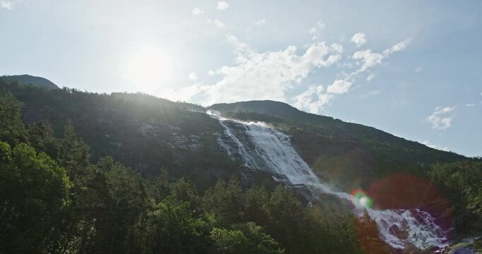 Langfossen waterfall backlit by the sun with lens flare over pine forest, Akrafjorden, Norway