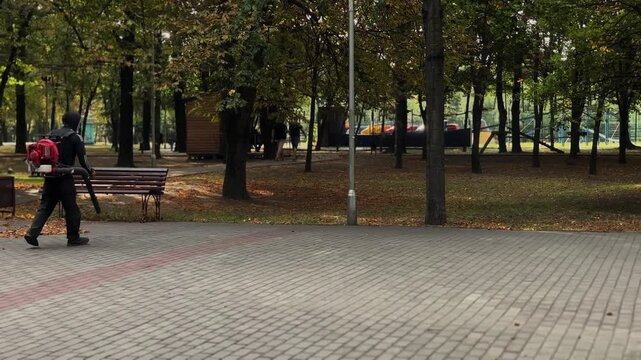 worker uses a leaf blower to clear leaves in a park