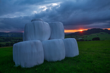 Bales of hay silage wrapped in protective film during a dramatic sunset