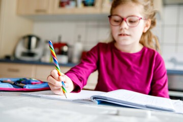 Little school girl learning at home. Elementary class student chid doing maths homework, writing...