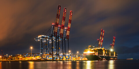 A massive container ship unloading at a container terminal in a seaport at night