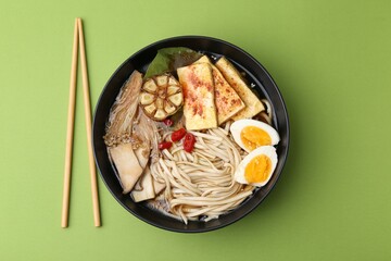 Tasty ramen with enoki and king oyster (eryngii) mushrooms in bowl on green table, flat lay