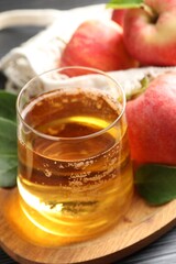 Fresh cider in glass, apples and green leaves on table, closeup