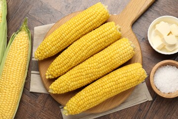 Tasty boiled corncobs, salt and butter on wooden table, flat lay